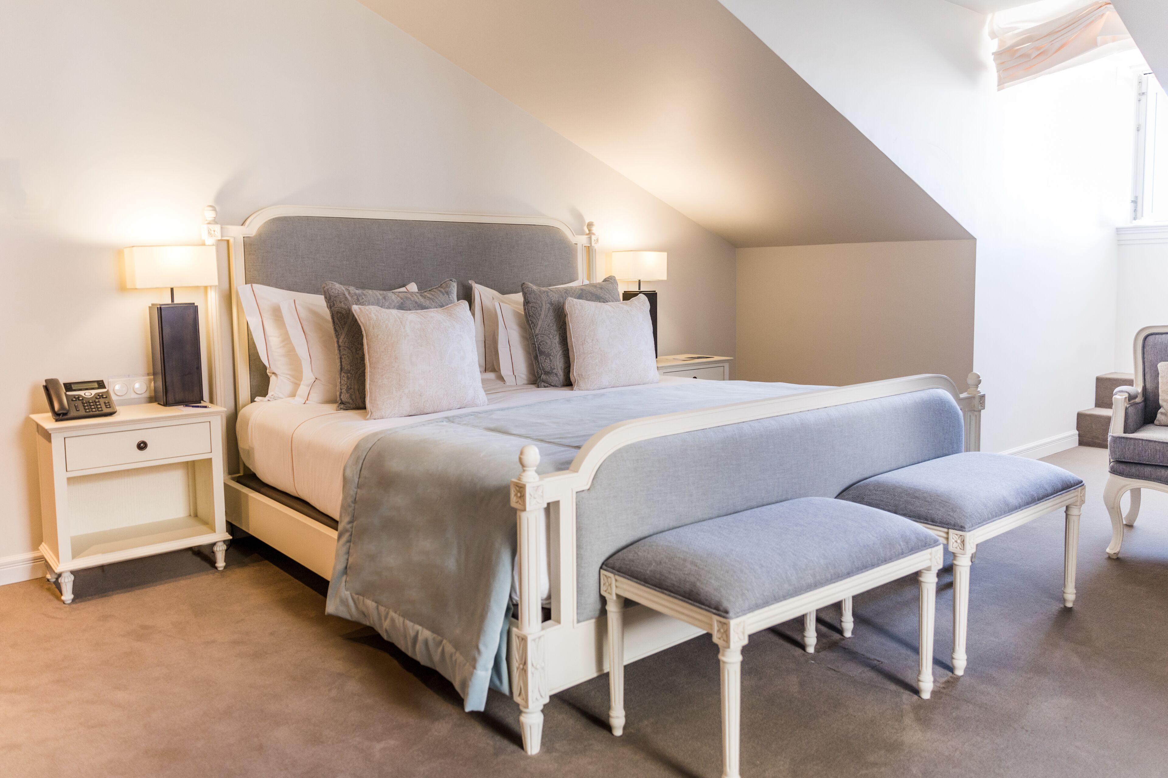 Une chambre à coucher avec un grand lit, deux tables de chevet, un banc et une chaise.