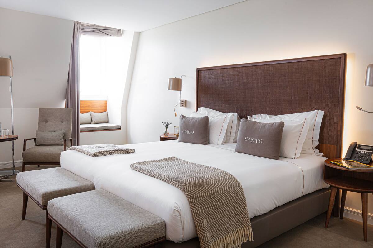 Une chambre d’hôtel avec un grand lit, deux tables de chevet, une chaise et une fenêtre avec des rideaux.