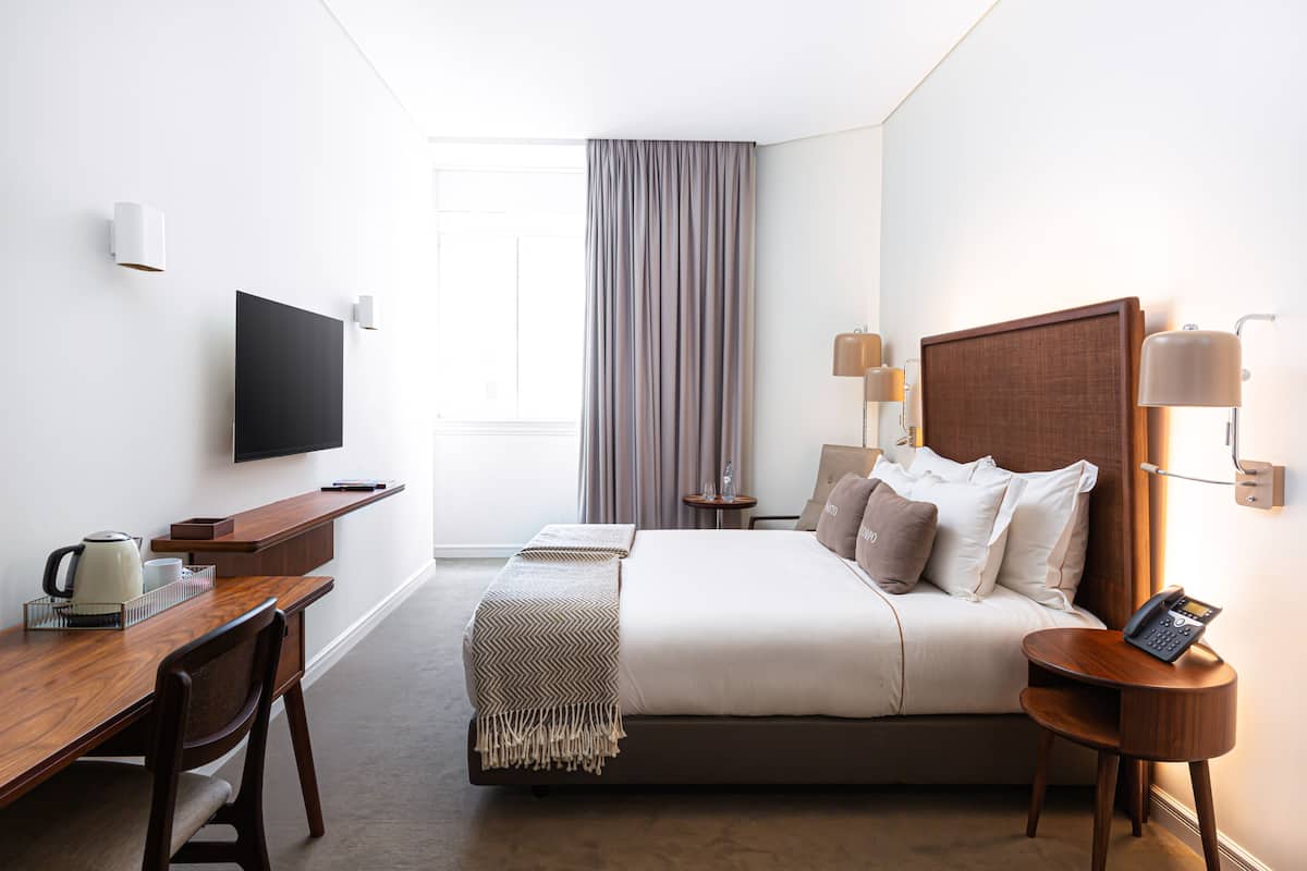 Une chambre d’hôtel comprenant un lit, une table de chevet, une lampe, une télévision, un bureau avec une bouilloire et une chaise.
