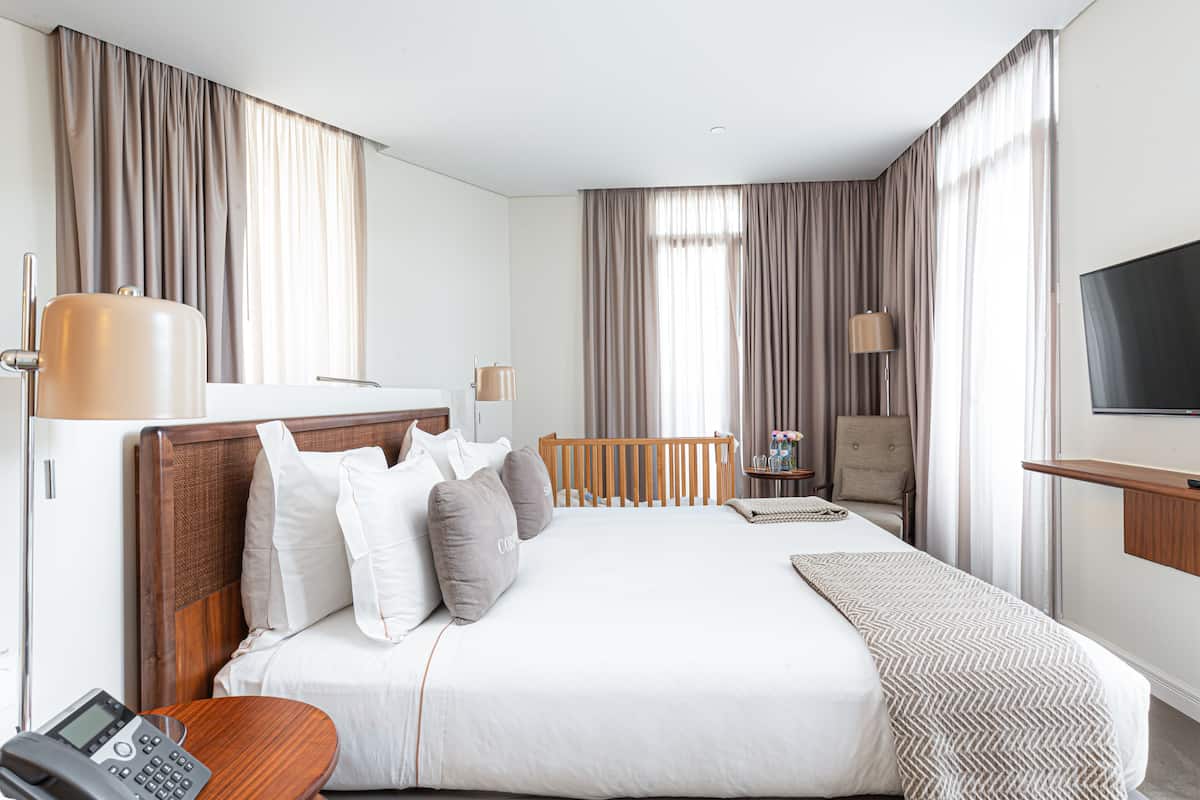 Une chambre d’hôtel avec un grand lit, une table de chevet, une lampe, une télévision et une salle de bain équipée de toilettes et d’un lavabo.