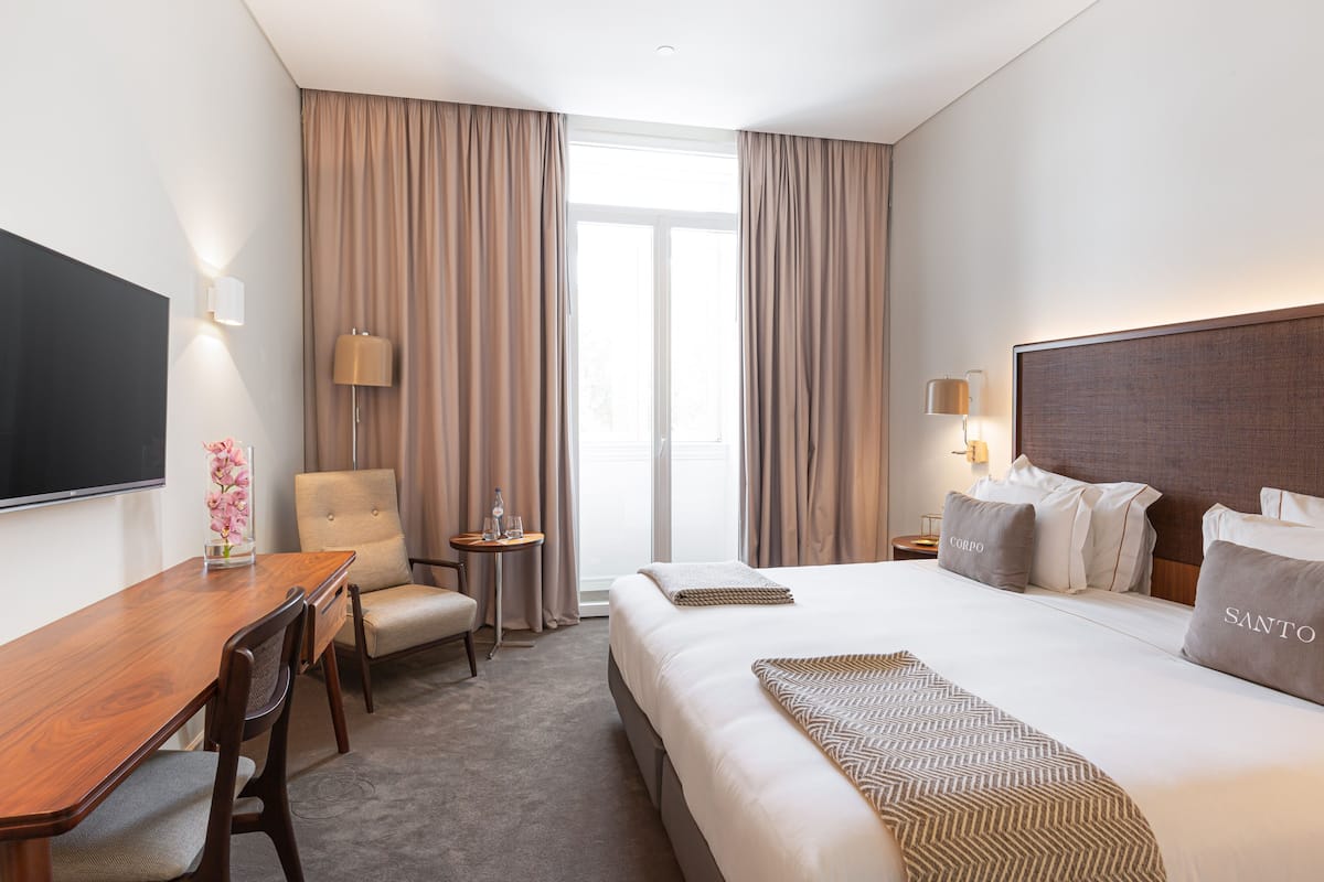 Une chambre d’hôtel avec un grand lit, un bureau, une chaise, une télévision et une fenêtre avec des rideaux.
