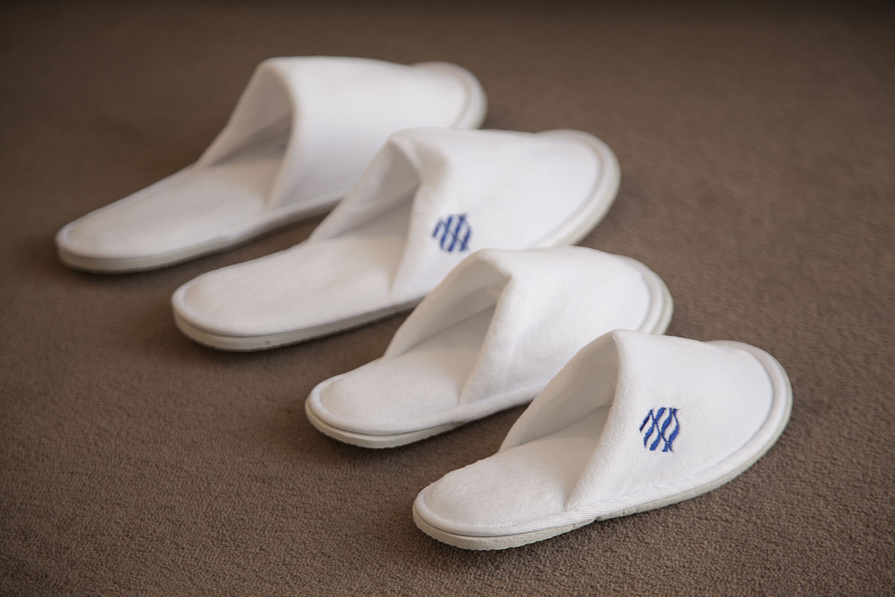 Un par de pantuflas blancas con bordados azules sobre un suelo alfombrado.