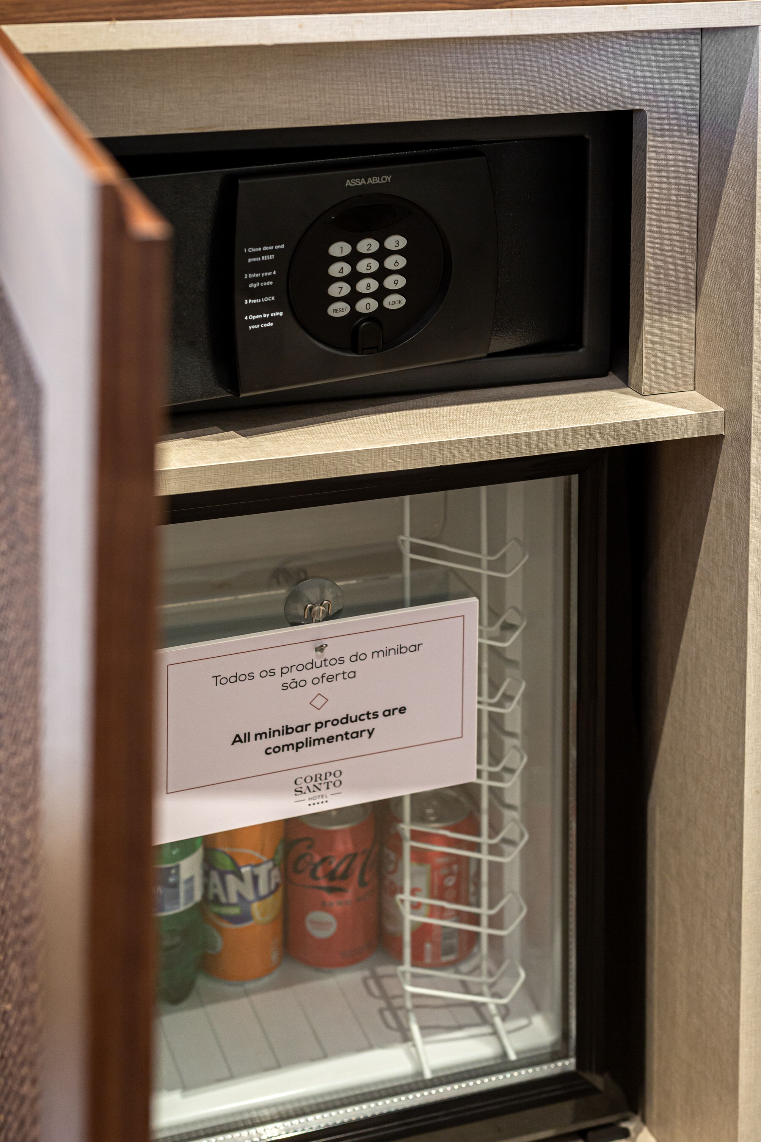 Een minibars kastje met een Coca-Cola en Fanta koelapparaat, een minibardeurtje en een bedieningspaneel voor de minibar.