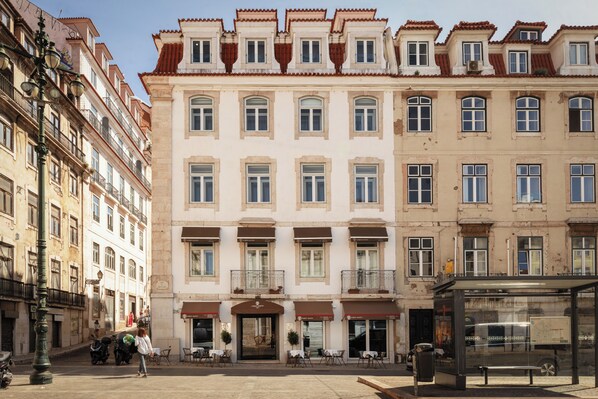 A multi-story building with a central entrance, balconies, and a bus stop. - Corpo Santo Lisbon Historical Hotel (Lisbon)