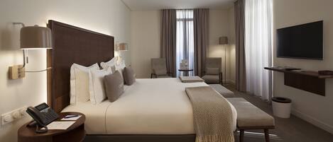 Une chambre d’hôtel avec un grand lit, des tables de chevet, un bureau avec un téléphone, une télévision et une fenêtre avec des rideaux.