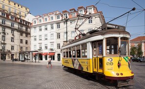 A yellow tram with "BEIRA" branding on the side, parked on a cobblestone street in an urban setting with buildings in the background. - Corpo Santo Lisbon Historical Hotel (Lisbon)