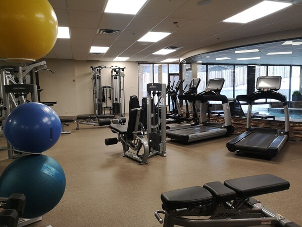 Un gimnasio con equipo de ejercicio, cintas de correr y un ventanal grande.