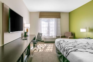 A hotel room with a bed, a desk with a chair, a TV, a lamp, and a window with curtains.