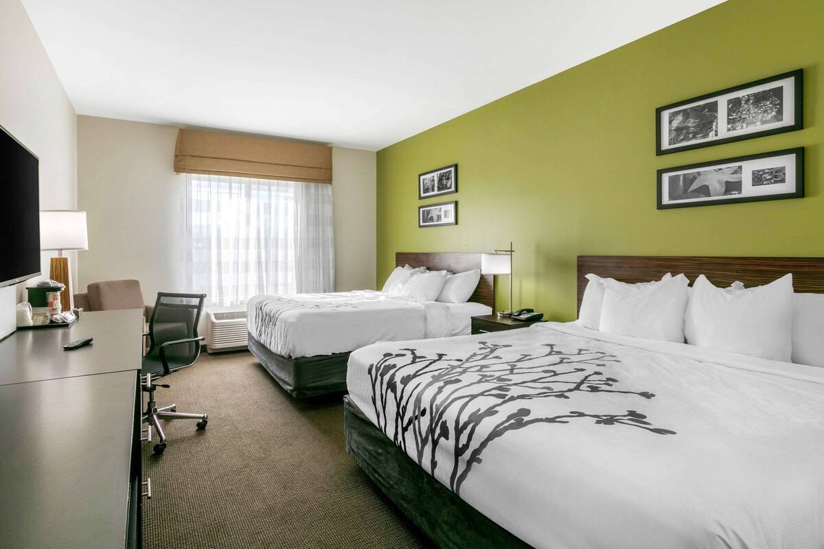Ett hotellrum med två sängar, ett skrivbord, en stol, en TV och inramade tavlor på väggen.