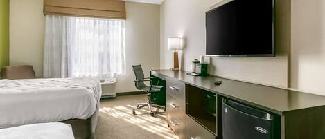 A hotel room with two beds, a desk, a chair, a television, and a minibar.