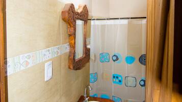 A bathroom with a wooden vanity, a mirror, a shower curtain with a geometric pattern, and a tiled floor.