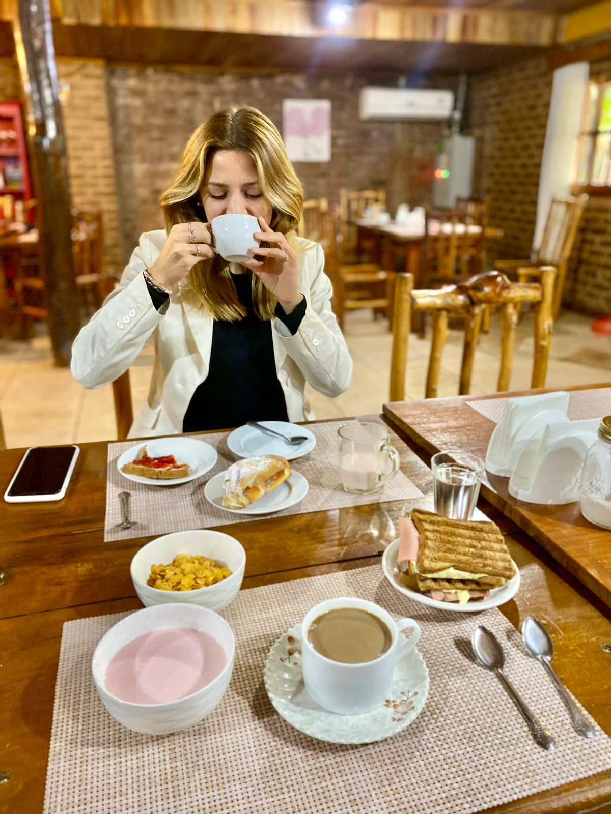 Una persona sentada en una mesa de madera con alimentos para el desayuno, como cereal, tostadas y una taza de café.