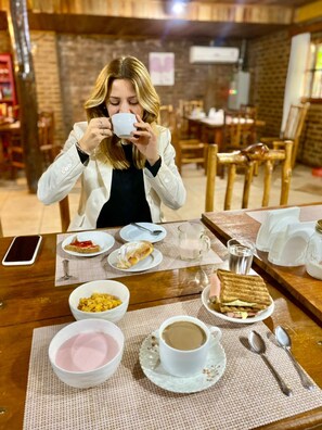 Une personne est assise à une table en bois devant un petit-déjeuner composé de céréales, de pain grillé et d’une tasse de café.
