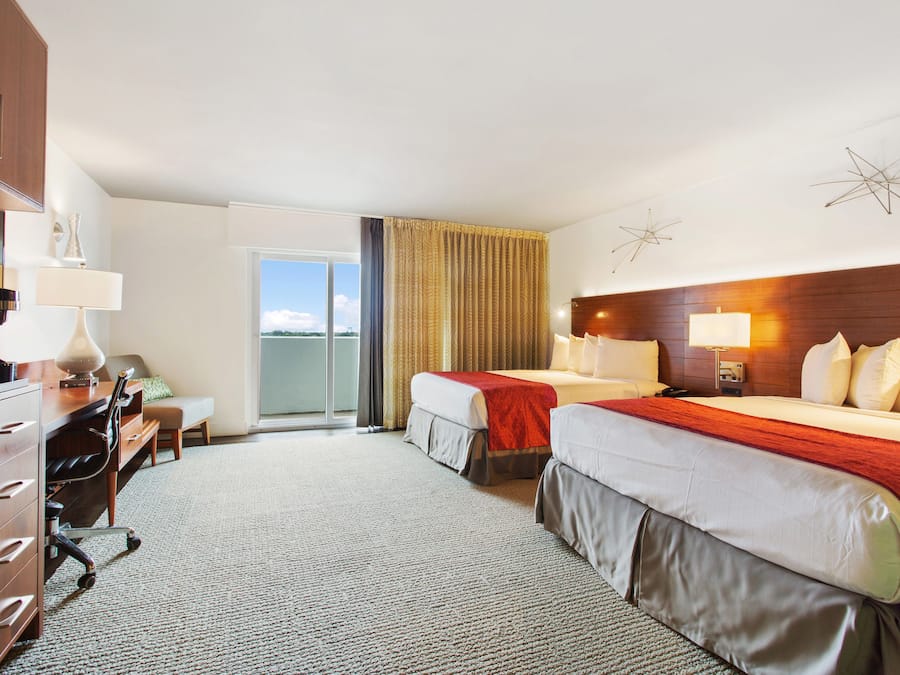 Ett hotellrum med två sängar, ett skrivbord, en stol, en byrå och utsikt över omgivningarna.