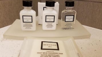 Una encimera de baño con tres botellas de revitalizante aire fresco Beekman 1801, una botella de champú Beekman 1801 y un paquete de jabón limpiador de leche de cabra Beekman 1801.