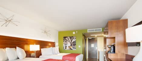 Ein Hotelzimmer mit zwei Betten, einem Schreibtisch, einem Sessel, einer Lampe und einem Gemälde an der Wand.