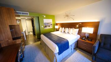 Una habitación de hotel con cama, mesita de noche, lámpara, silla y pared verde.