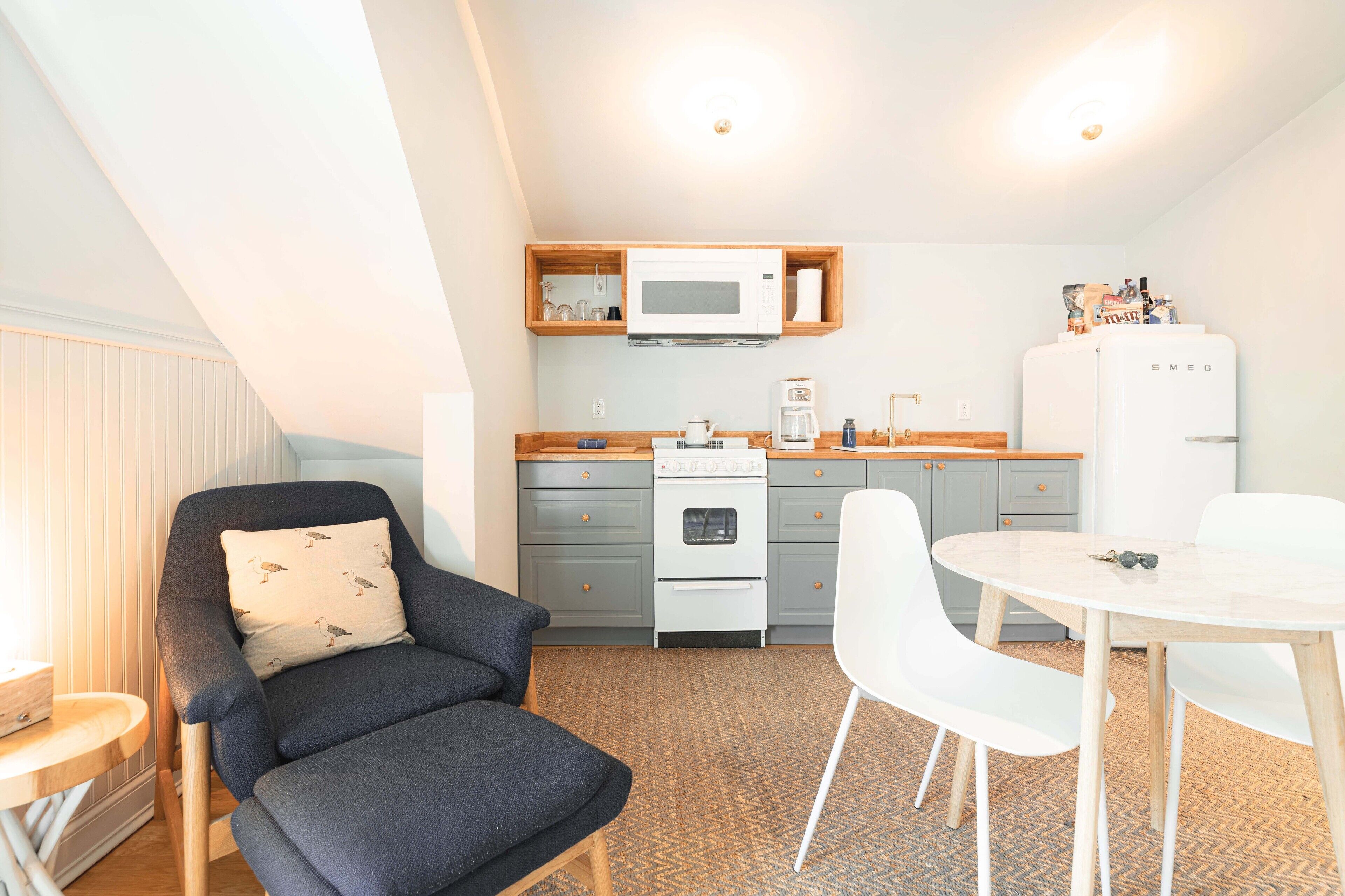 A compact kitchen with a microwave, stove, and refrigerator. There is a dining table with chairs and a sofa with a cushion.