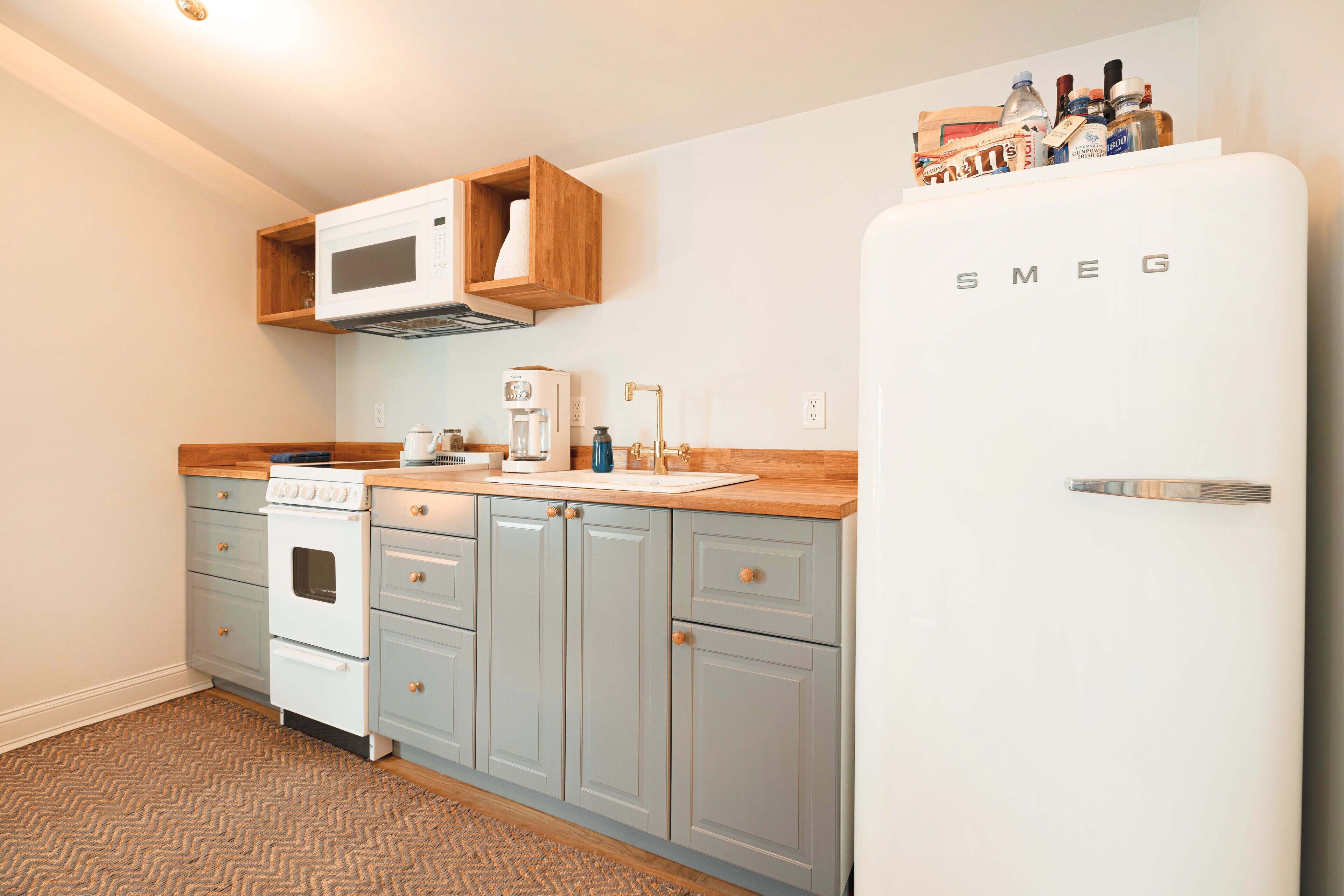 A compact kitchen with a white refrigerator, a microwave, a coffee maker, and wooden cabinets.