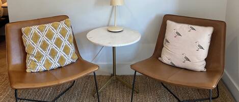 A room with two brown chairs, a small round table with a lamp, and a framed bird artwork on the wall.