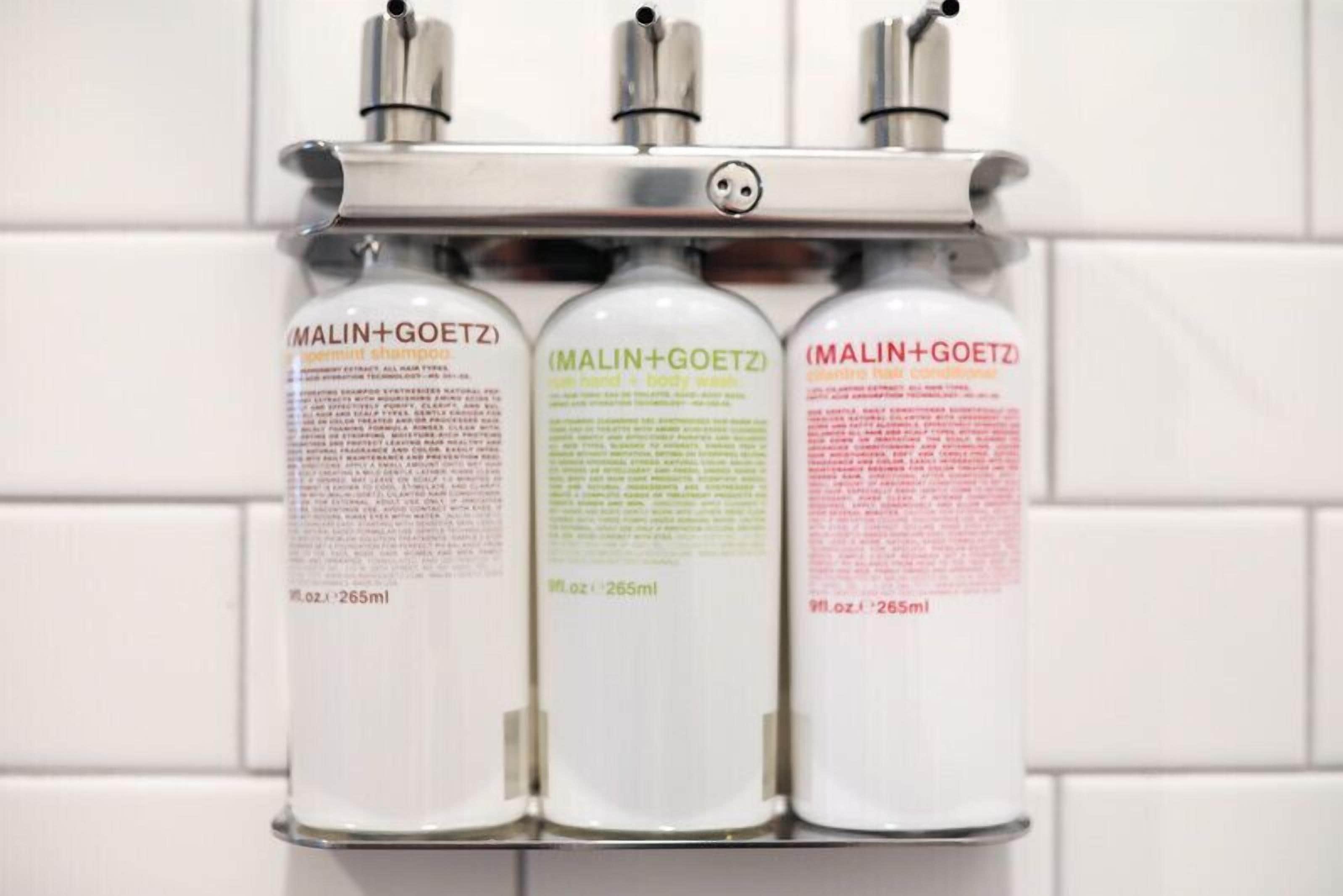 Three bottles of MALIN+GOETZ shampoo on a wall-mounted dispenser.