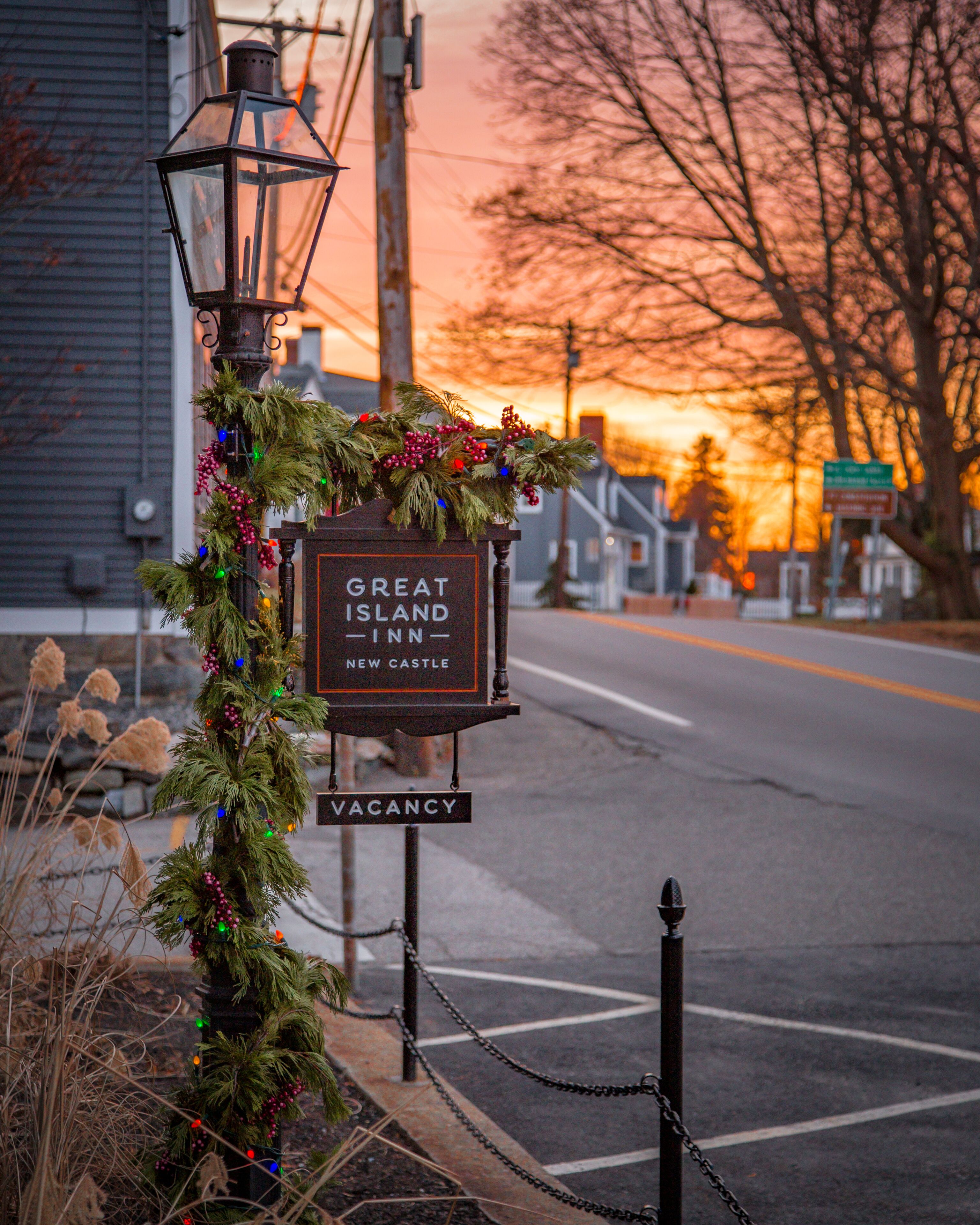 A Great Island Inn sign with a 'VACANCY' label, decorated with evergreen and berries, located at the roadside.