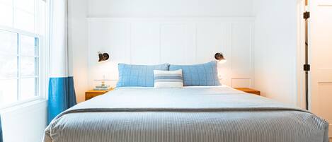 A neatly made bed with a striped bedspread, two blue pillows, and two bedside lamps.