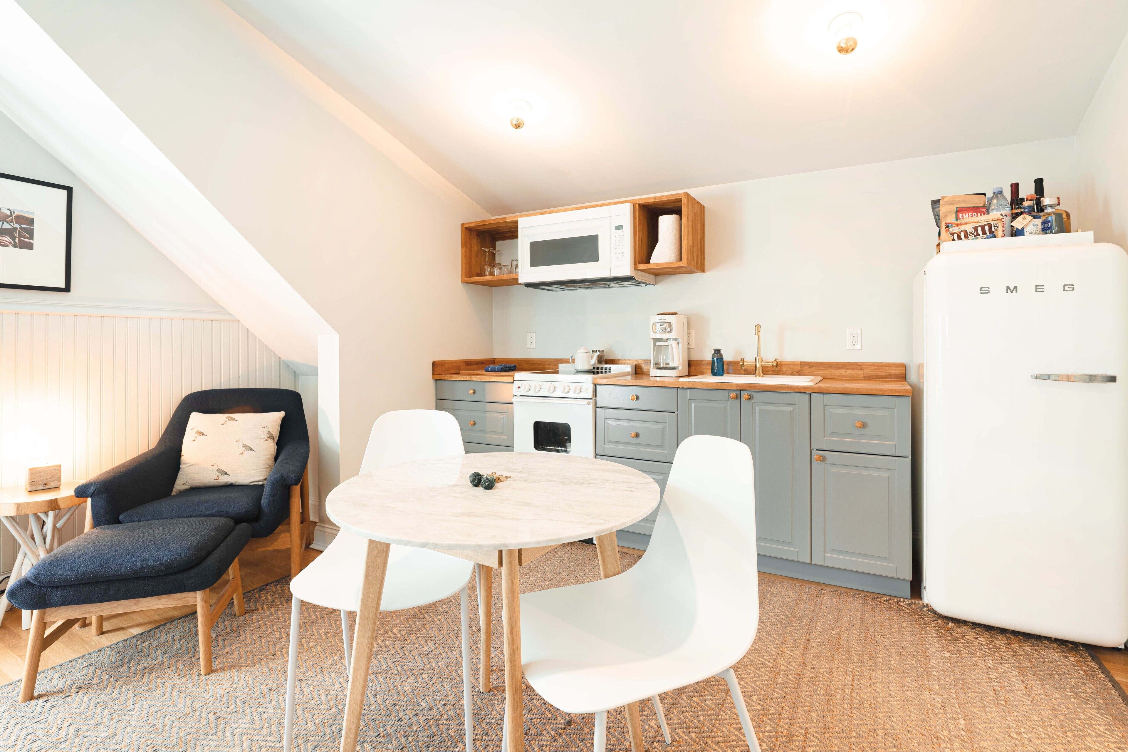 Une cuisine compacte équipée d’un four à micro-ondes, d’une cuisinière et d’un réfrigérateur. On y trouve une table à manger avec des chaises et un banc rembourré.