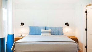 Een netjes opgemaakt bed met een gestreepte sprei en twee kussens, aan weerszijden met nachtkastjes en lampen, in een kamer met een houten vloer en witte muren.
