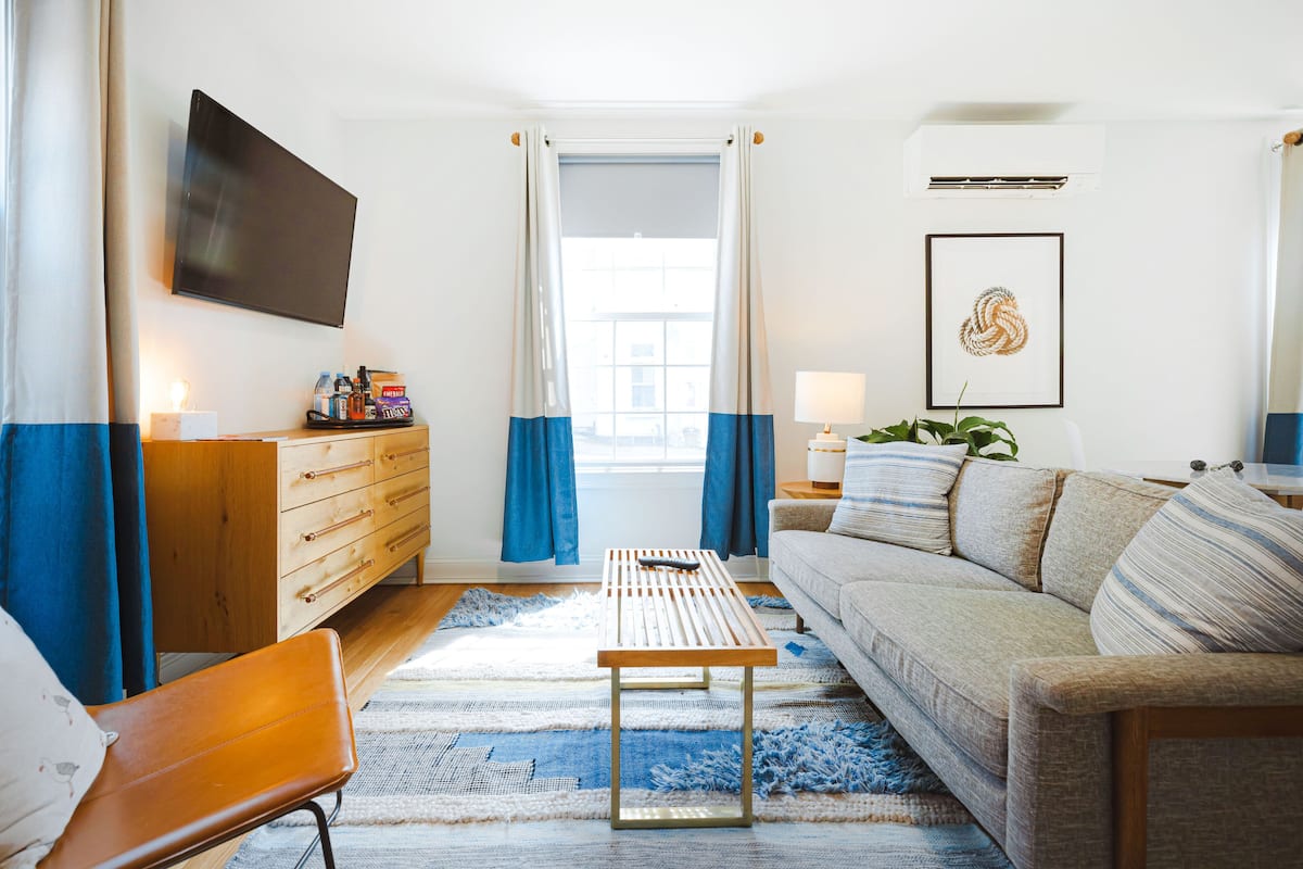 Ein modernes Wohnzimmer mit Sofa, Couchtisch, Fernseher und Blick durch ein Fenster.