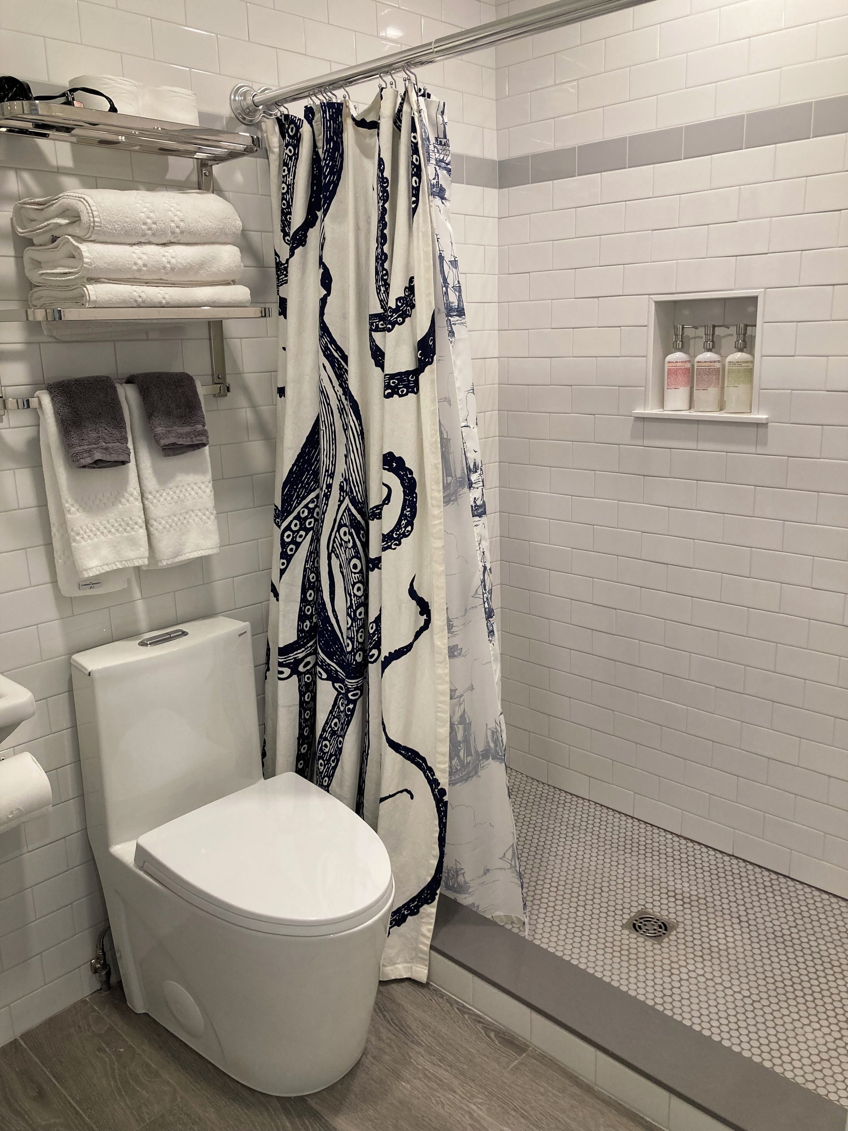 A modern bathroom with a white toilet, a shower with a patterned curtain, and a shelf with toiletries.