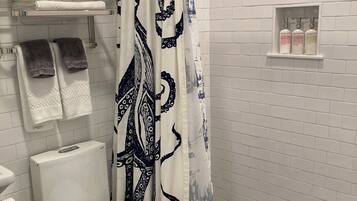 A modern bathroom with a white toilet, a shower with a patterned curtain, and a shelf with toiletries.