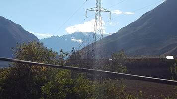 Paisaje montañoso con una torre de líneas eléctricas y un edificio con techo de tejas.