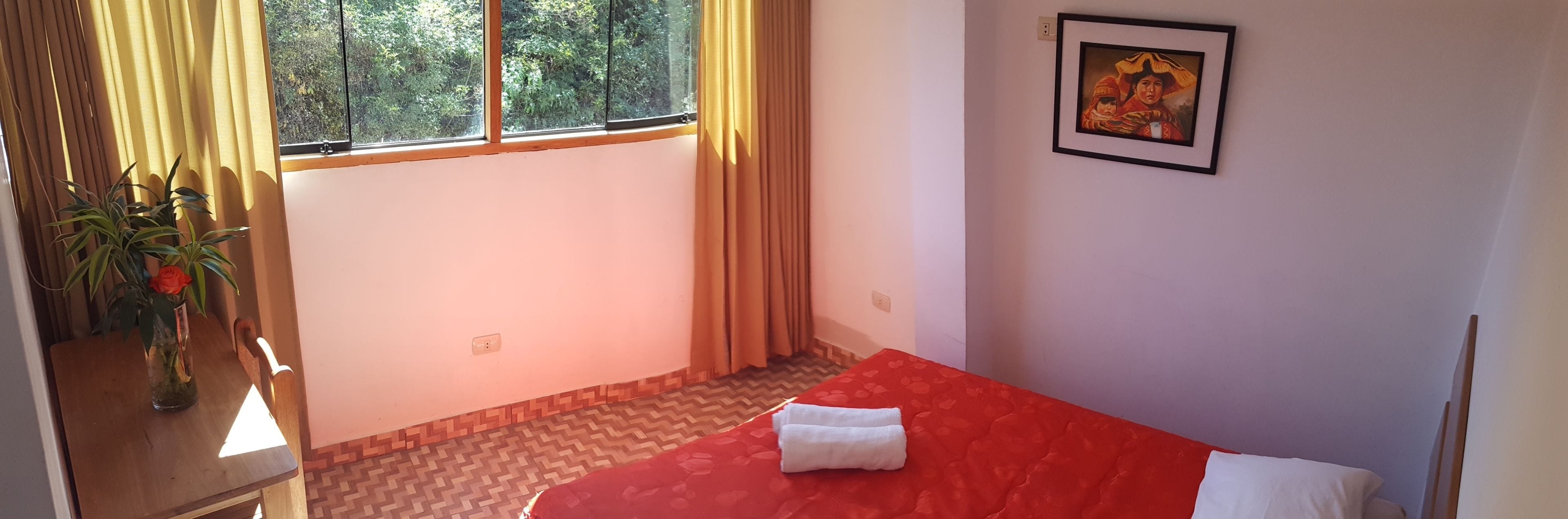A room with a bed, a window with curtains, a painting on the wall, and a potted plant.