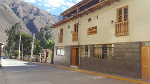A building with a sign indicating it is a hostel, featuring a stone facade, wooden balconies, and a mountain backdrop. - Tambo de Ollantay (Ollantaytambo)