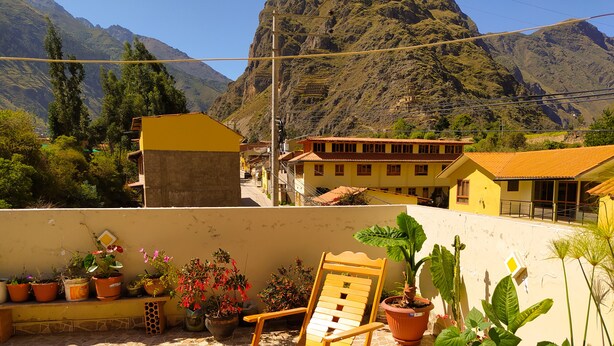 A terrace with a wooden chair, potted plants, and a mountain view. - Tambo de Ollantay (Ollantaytambo)