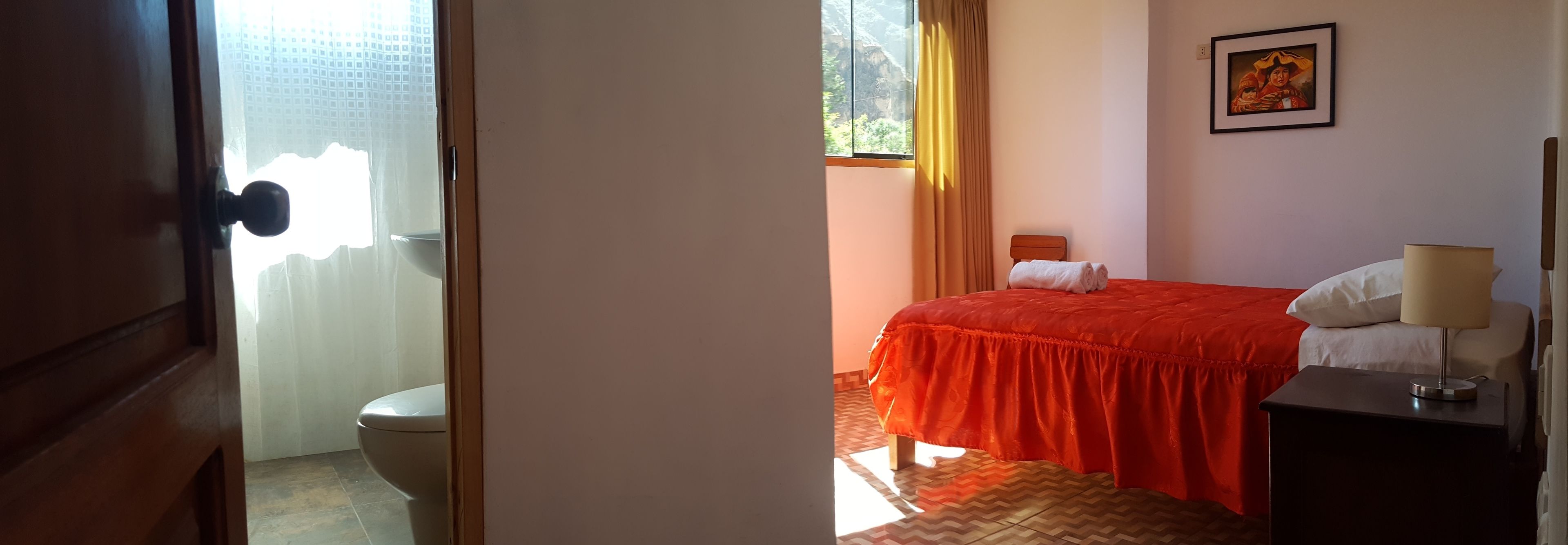 Une chambre d’hôtel avec un lit, une table de chevet avec une lampe, une fenêtre avec des rideaux et un tableau au mur.