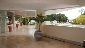 Un amplio espacio interior con una planta grande en maceta, una piscina visible a través del muro de cristal y un suelo de baldosas.