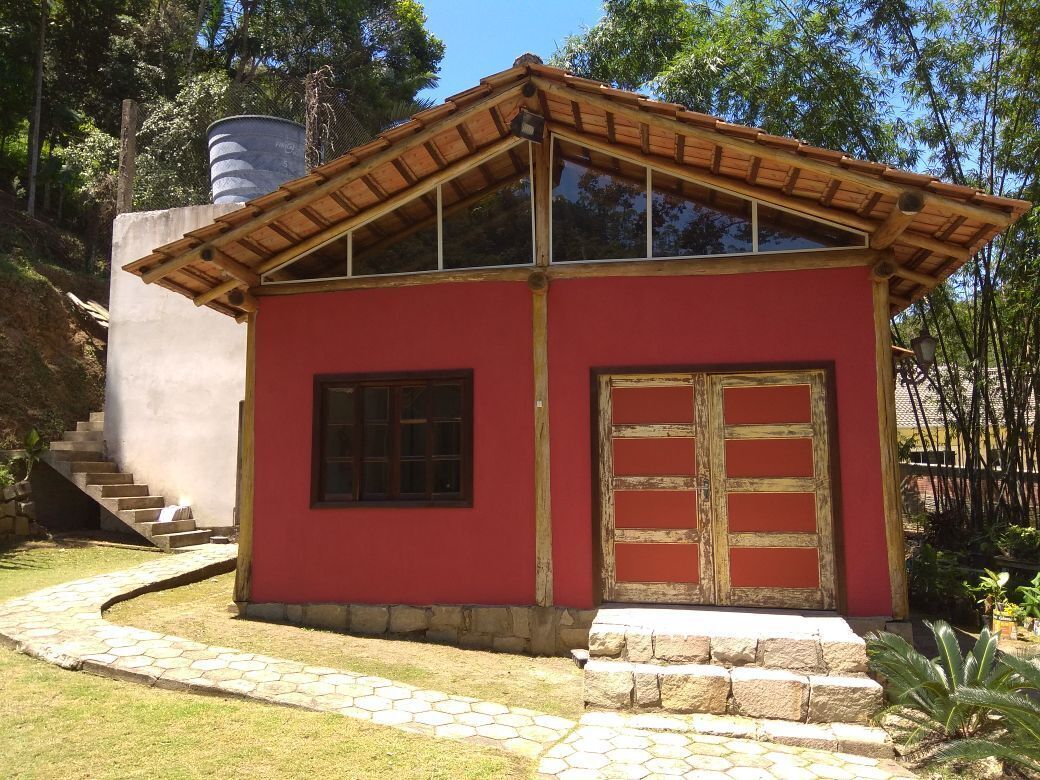 Un pequeño edificio rojo con techo de madera, un ventanal grande y una puerta de madera.