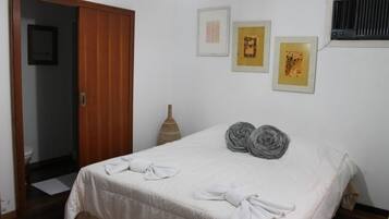 Un dormitorio con cama, toallas, una puerta, aire acondicionado instalado en la pared y cuadros enmarcados.