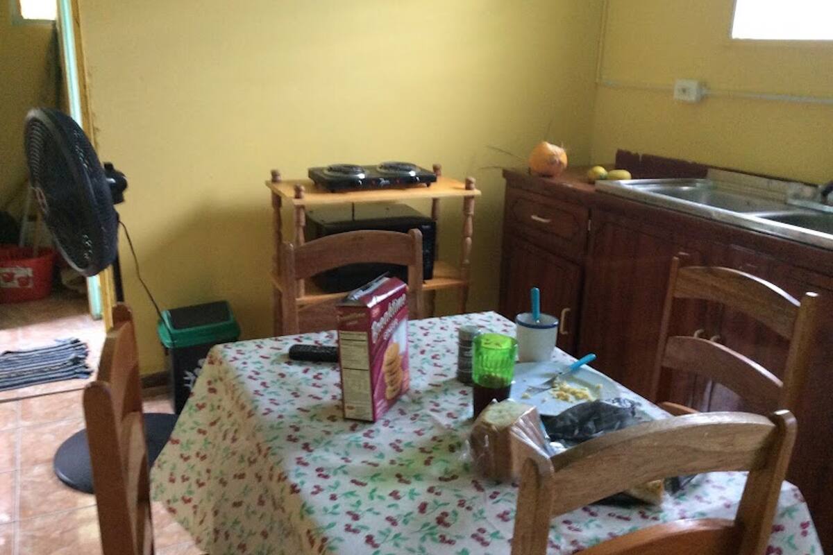 A small kitchen with a table, chairs, a fan, and basic appliances.