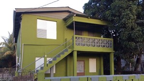 A two-story building with a green exterior, a balcony, and a staircase leading to the second floor. - MaFlo Arms Apartments (Belize City)