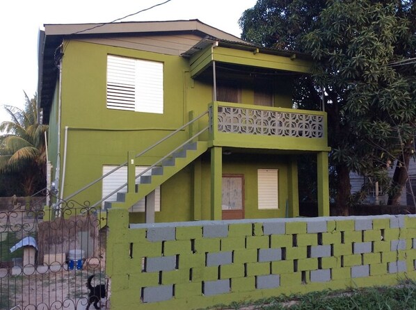 Un immeuble de deux étages, à la façade verdoyante, doté d’un balcon et d’un escalier menant au deuxième étage.