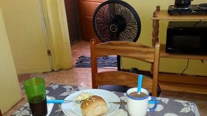 A dining table with a plate of food, a cup with a straw, and a green glass. - MaFlo Arms Apartments (Belize City)