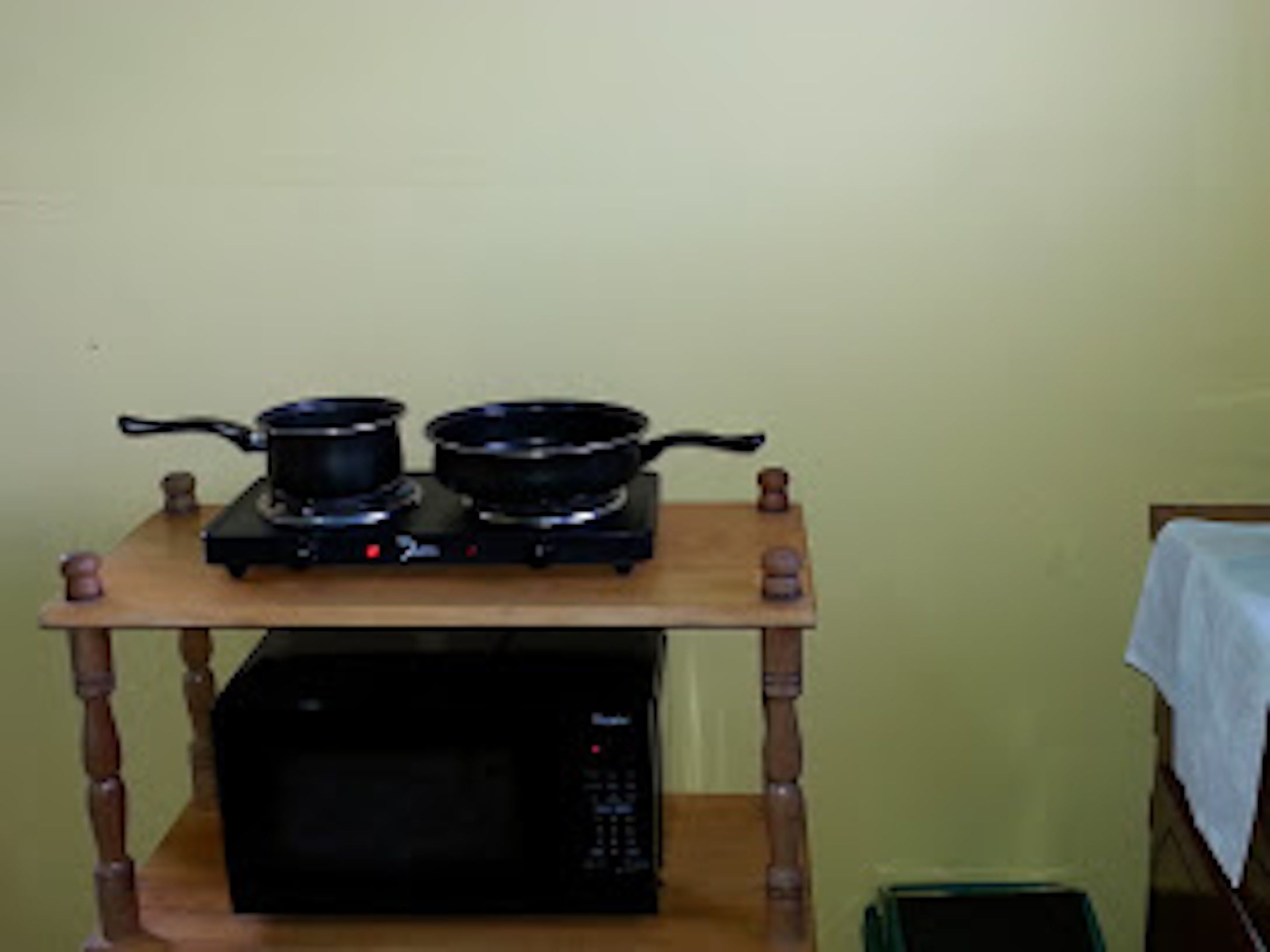 Uma cozinha com micro-ondas, uma mesa de madeira com duas panelas em uma placa e uma lixeira verde.