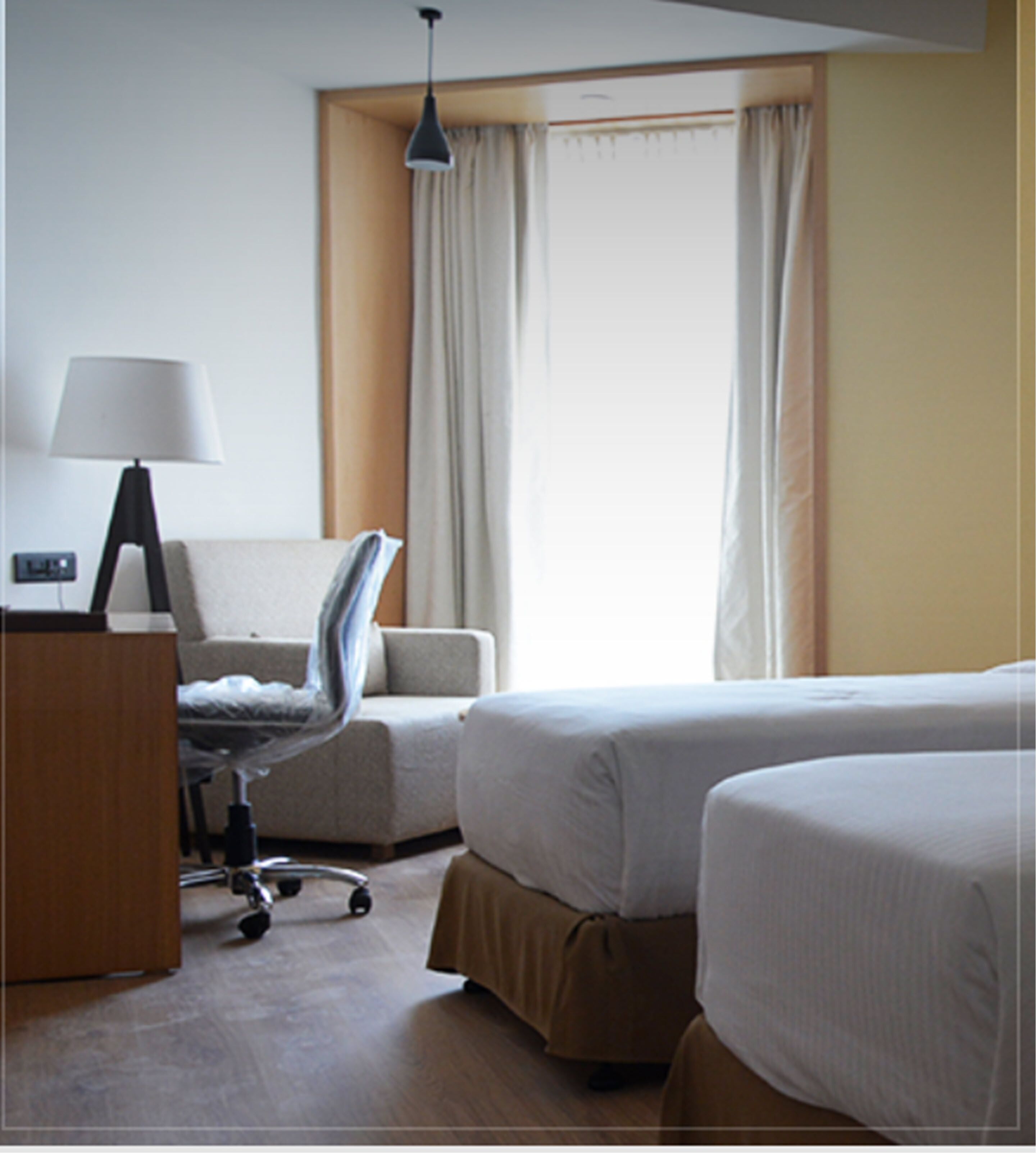 A hotel room with a bed, a desk, a chair, and a lamp.