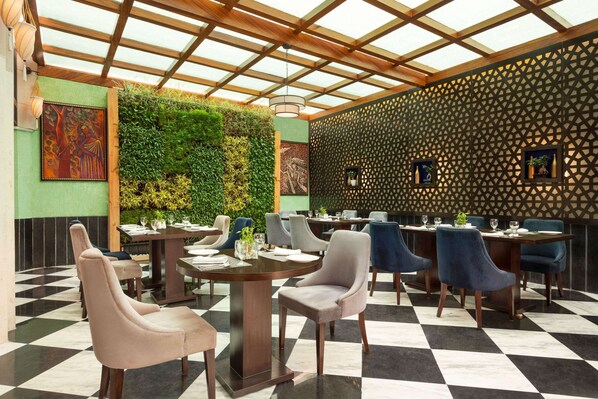Restaurante con suelo a cuadros, techo de madera y pared vertical con jardín. Las mesas están dispuestas con sillas y centros de mesa.