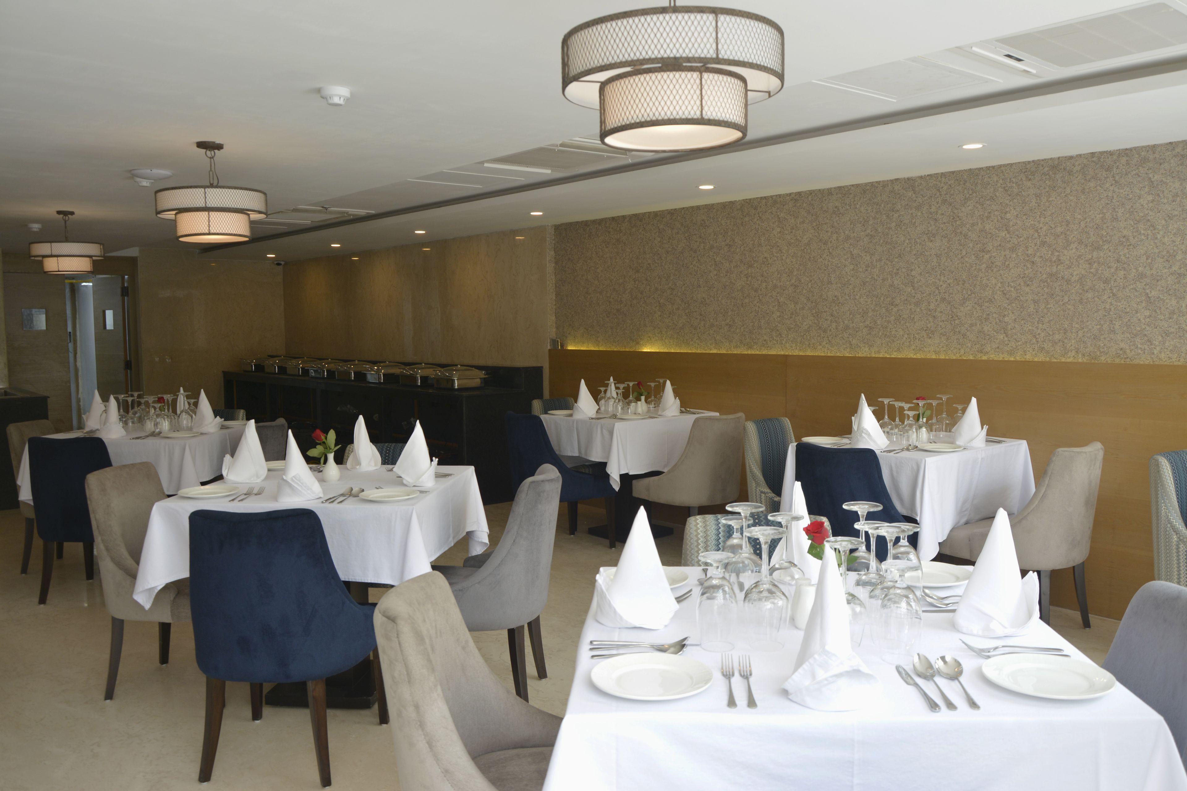 A dining area with tables set for service, chairs, and a bar area in the background.