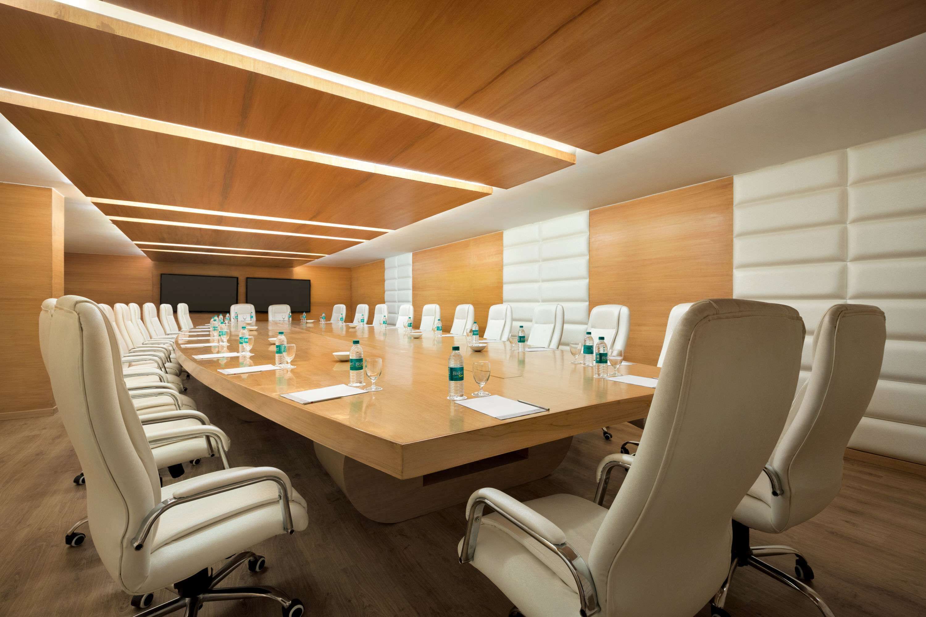 A conference room with a long table, white chairs, and wooden panel walls.