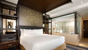 Ein Hotelzimmer mit einem großen Bett, einem Holzkopfstück, einer Wand mit Dekoration, einer Duschkabine aus Glas und Blick ins Badezimmer.